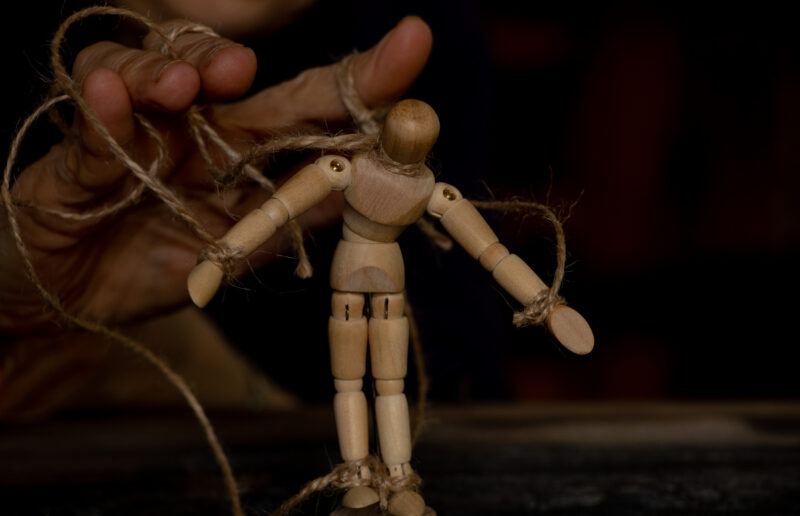 a wooden man on ropes tied to a mans hand manipulation of people and slavery free will power