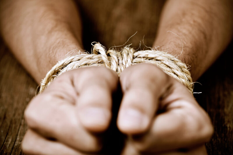 the hands of a young man tied with rope