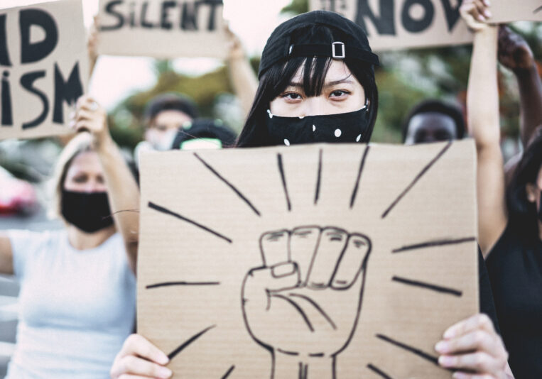 Asian girl wearing face mask while protest against racism on city street - Equal rights for people and demonstration concept - Focus on eyes